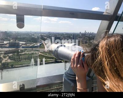 Une belle fille regarde le paysage, un panorama de la ville dans la salle d'observation, une paire de jumelles, un télescope avec un accepteur de facture sur un Banque D'Images