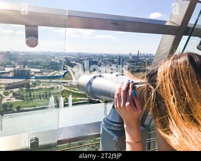 Une belle fille regarde le paysage, un panorama de la ville dans la salle d'observation, une paire de jumelles, un télescope avec un accepteur de facture sur un Banque D'Images