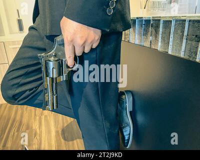 un homme dans un costume festif et des chaussures lisses en cuir verni tient un pistolet. pistolet noir, petit et compact. arme militaire. agent spécial en mission. Banque D'Images