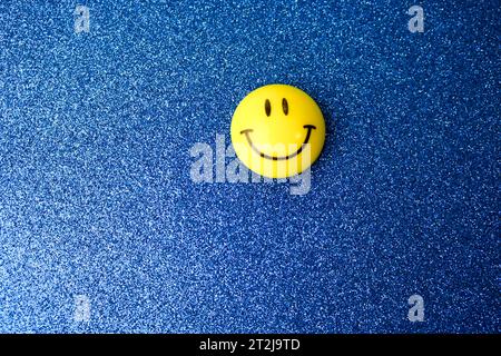 Plastique rond jaune souriant joyeux jouet sourire rond visage Emoji sur un fond bleu. Banque D'Images