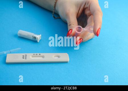 un récipient en plastique rose pour la collecte de sang. une fille avec une manucure rouge tient une petite forme pour prendre du sang dans ses mains. l'autodiagnostic du viru Banque D'Images