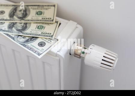 Pile de billets de banque en dollars sur la batterie du radiateur de chauffage avec thermostat. Concept de coûts de chauffage coûteux et de facture énergétique croissante Banque D'Images