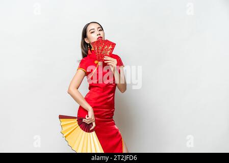 Femme asiatique en costume de cheongsam oriental tenant des enveloppes rouges Ang Pow et fan posant sur fond de studio gris clair pour les concepts du nouvel an chinois, Banque D'Images