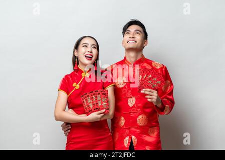 Couple asiatique en costumes orientaux traditionnels tenant des enveloppes rouges ou Ang Pow en fond gris pour les concepts du nouvel an chinois, les textes étrangers signifient gr Banque D'Images