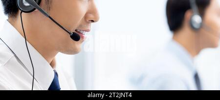 Vue latérale de consultants masculins asiatiques dans des casques avec microphone parlant avec des clients tout en travaillant dans un bureau de centre d'appels Banque D'Images