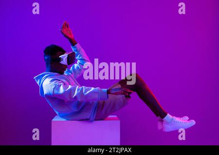 Jeune homme africain portant casque en verre VR sur fond futuriste violet cyberpunk néon Banque D'Images