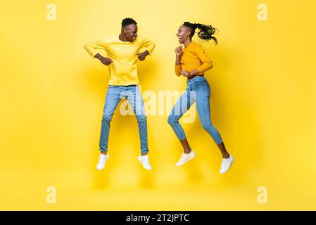 Joyeux souriant jeune couple afro-américain sautant dans fond de studio isolé jaune Banque D'Images