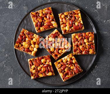 barres sablées aux noix mélangées au caramel sur plaque noire sur table en béton gris, vue horizontale d'en haut, mise à plat, gros plan Banque D'Images