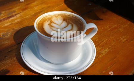 Le café avec de la mousse artistique sur le dessus est servi sur une table en bois Banque D'Images