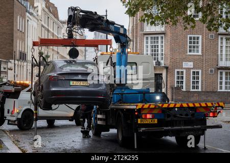 Une voiture Tesla stationnée illégalement et bloquée est soulevée sur un camion de remorquage à Victoria, le 20 octobre 2023, à Londres, en Angleterre. Banque D'Images