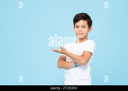 Mignon garçon souriant en t-shirt blanc Uni ouvrant la main vide dans le studio isolé fond de couleur bleu clair Banque D'Images