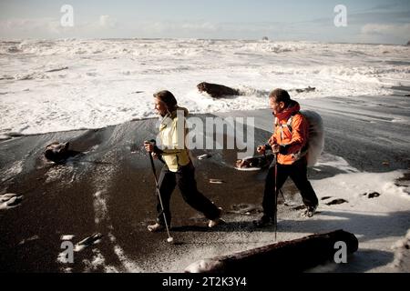 Un homme et une femme marchent le long de la rive de la plage du Rialto tandis que d'énormes vagues lavent l'écume de mer sur le sable. Banque D'Images