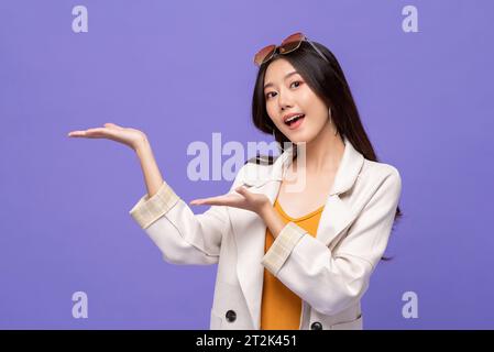 Tour de taille vers le haut protrait de jolie femme asiatique souriant et ouvrant les mains vides de côté dans fond de studio de couleur violet isolé Banque D'Images