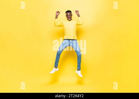 Homme africain excité surpris sautant avec les mains levées dans le fond isolé de couleur jaune studio Banque D'Images