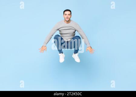 Amusant énergique beau jeune homme caucasien sautant comme une grenouille dans fond de studio isolé de couleur bleu clair Banque D'Images