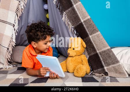 Photo de garçon d'enfant intelligent finir de faire ses devoirs montrer le jouet copybook dans la tente de couverture isolé fond de couleur bleue Banque D'Images