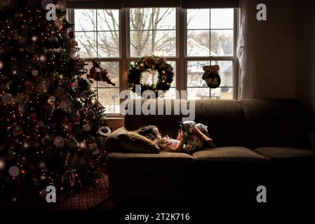 Petite fille allongée sur le canapé jouant avec la technologie à noël Banque D'Images