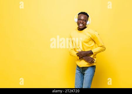 Positif heureux homme africain écoutant de la musique sur des écouteurs en fond isolé de studio de couleur jaune avec espace de copie Banque D'Images