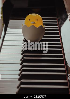 Dessin animé bébé poussin assis dans le support d'oeuf cassé sur le clavier de piano. Jaune mignon poulet éclosion de l'œuf, espace pour le texte, mise au point sélective. Banque D'Images