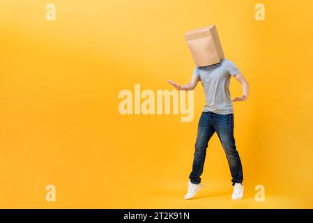 Homme anonyme avec la tête couverte de sac en papier ouvrant les mains dans le fond jaune de studio isolé avec l'espace de copie Banque D'Images