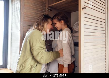 Une maman attrayante et son bébé mignon font les tâches ménagères. Une jeune femme et sa fille chargent une machine à laver. Une adorable mère l'embrasse éclairée Banque D'Images