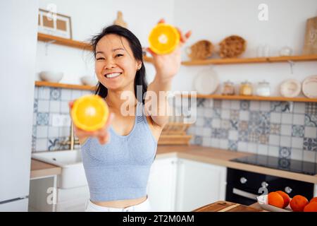 Une jeune femme asiatique séduisante sourit et montre des oranges à la caméra. Une charmante dame coréenne prépare du jus d'orange. Une belle fille thaïlandaise se prépare Banque D'Images