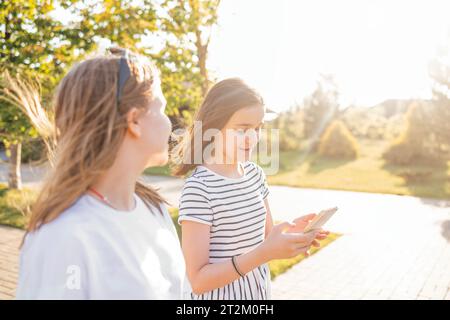 Deux adolescentes marchent dans la rue et bavardent en été. Une fille mignonne dans des vêtements décontractés montre un smartphone à son amie. Adolescents sm Banque D'Images