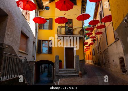 Rue de la ville à Porto Ceresio avec parasols suspendus dans une journée d'été ensoleillée à Porto Ceresio, Lombardie, Italie Banque D'Images