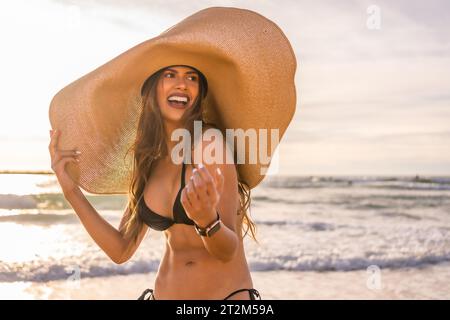 Heureuse jeune femme portant un chapeau de soleil sur la plage pendant le coucher du soleil Banque D'Images