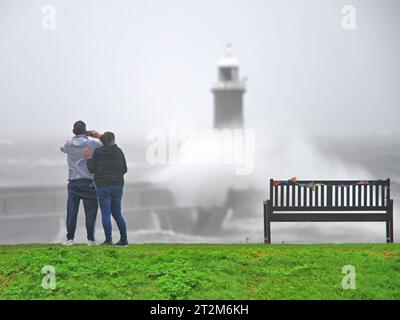 Deux personnes regardent les vagues qui s'écrasent sur le phare de North Pier à Tynemouth pendant la tempête Babet vendredi 20 octobre 2023 Banque D'Images