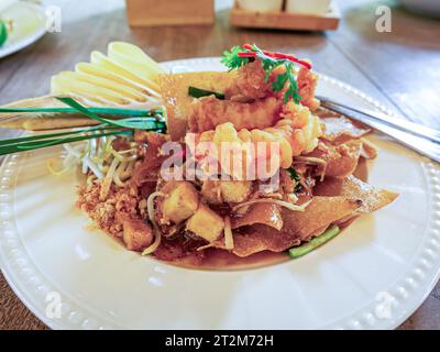 Vue latérale de délicieux wontons croustillants sautés avec crevettes frites, coriandre fraîche, citron et germes de haricots dans une assiette en céramique. Thai style phad TH Banque D'Images