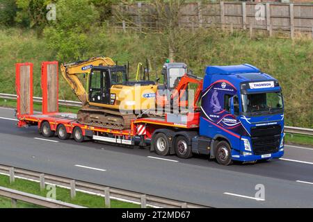 Thompson Warehousing & distribution 2019 Volvo Diesel 12777 cc rouck remorque. Lowloader transportant des équipements de construction de la Pelle hydraulique 313F ; se déplaçant à grande vitesse sur l'autoroute M6 dans le Grand Manchester, Royaume-Uni Banque D'Images