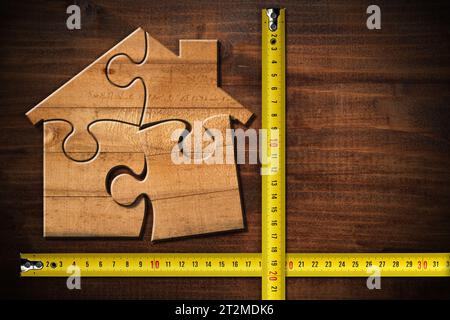 Maison en bois faite de pièces de puzzle sur un établi en bois avec deux rubans à mesurer et espace de copie. Amélioration de l'habitat et concept de l'industrie de la construction. Banque D'Images