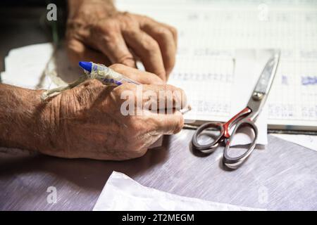 Gros plan d'une main tenant un stylo dans un livre. Main d'homme âgé faisant le travail comptable manuellement. Concept de vieillissement actif, écriture manuscrite. Image horizontale. Banque D'Images