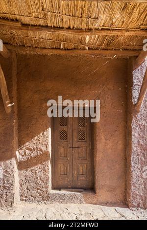 L'image montre une porte marocaine traditionnelle avec un motif géométrique sculpté dans le bois. La porte est placée dans un mur de briques de boue rouge-brun avec un diago Banque D'Images