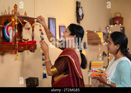 Joyeuse fille indienne aidant la mère pour la décoration du festival diwali de pooja mandir ou mandap à la maison - concept de lien familial, de dévotion et Banque D'Images