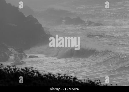 Vagues brisantes et embruns balayés par le vent. Près de la plage de Poldhu, Poldhu Cove, Cornwall. Une crique populaire pour les surfeurs et les débutants. Pas dans ces mers bien sûr. Banque D'Images