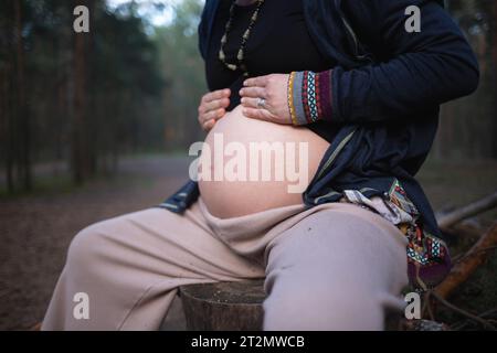 une femme enceinte est assise sur une bûche dans la forêt et embrasse son ventre. Banque D'Images