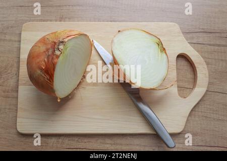 Un gros oignon jaune coupé en deux sur une planche à découper en bois avec un couteau allongé à proximité, gros plan Banque D'Images