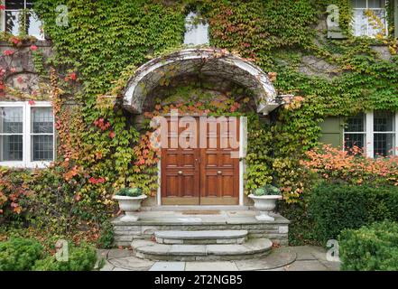 Façade de la vieille maison couverte de lierre avec élégantes portes doubles grain de bois Banque D'Images