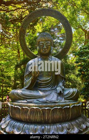 Statue de Bouddha avec palmier surélevé et jardin de la nature verdoyante derrière elle Banque D'Images