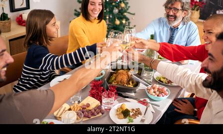 Acclamations famille riant célébrant le repas de Noël ensemble griller avec du vin sur la table à la maison. Banque D'Images