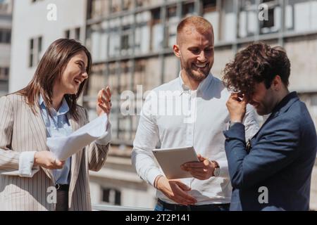 Les gens d'affaires ayant une conversation amusante et riant tout en travaillant à distance à l'extérieur sur une journée ensoleillée Banque D'Images