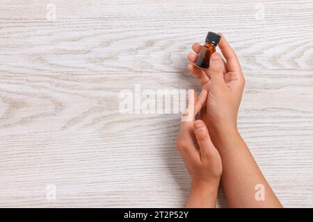 Femme avec bouteille d'huile essentielle sur fond en bois, vue de dessus et espace pour le texte Banque D'Images