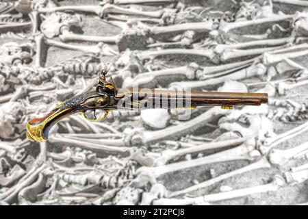 Pistolet à silex historique, sur un arrière-plan flou squelettes des soldats du champ de bataille médiéval Banque D'Images