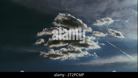 Paysage nuageux hypnotique sous un ciel bleu profond et un avion à réaction qui tranche à travers le ciel laissant une traînée de condensation blanche pure. Banque D'Images