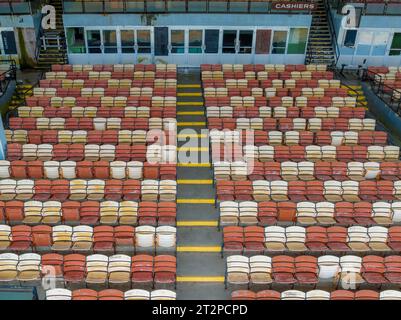 Vieux sièges en bois peints orange et jaune délavé dans une tribune abandonnée d'un stade. Banque D'Images