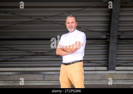 Portrait de trois quarts du corps d'un homme aux cheveux gris attrayant avec un T-shirt blanc a les bras croisés, porte une montre élégante, et semble amical à t Banque D'Images