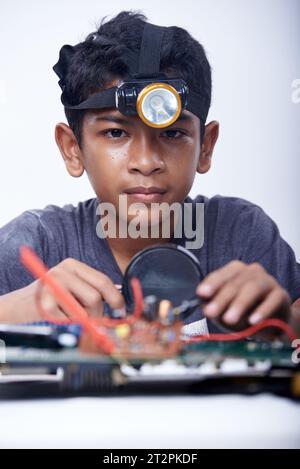 Jeune écolier utilisant une loupe travaillant sur une carte mère d'ordinateur dans un laboratoire d'école électronique Banque D'Images
