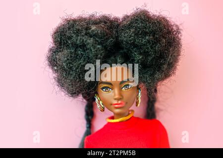 9 octobre 2023. Barnaul, Russie : poupée Barbie afro-américaine avec les cheveux noirs dans un costume rouge debout sur un fond rose. Banque D'Images